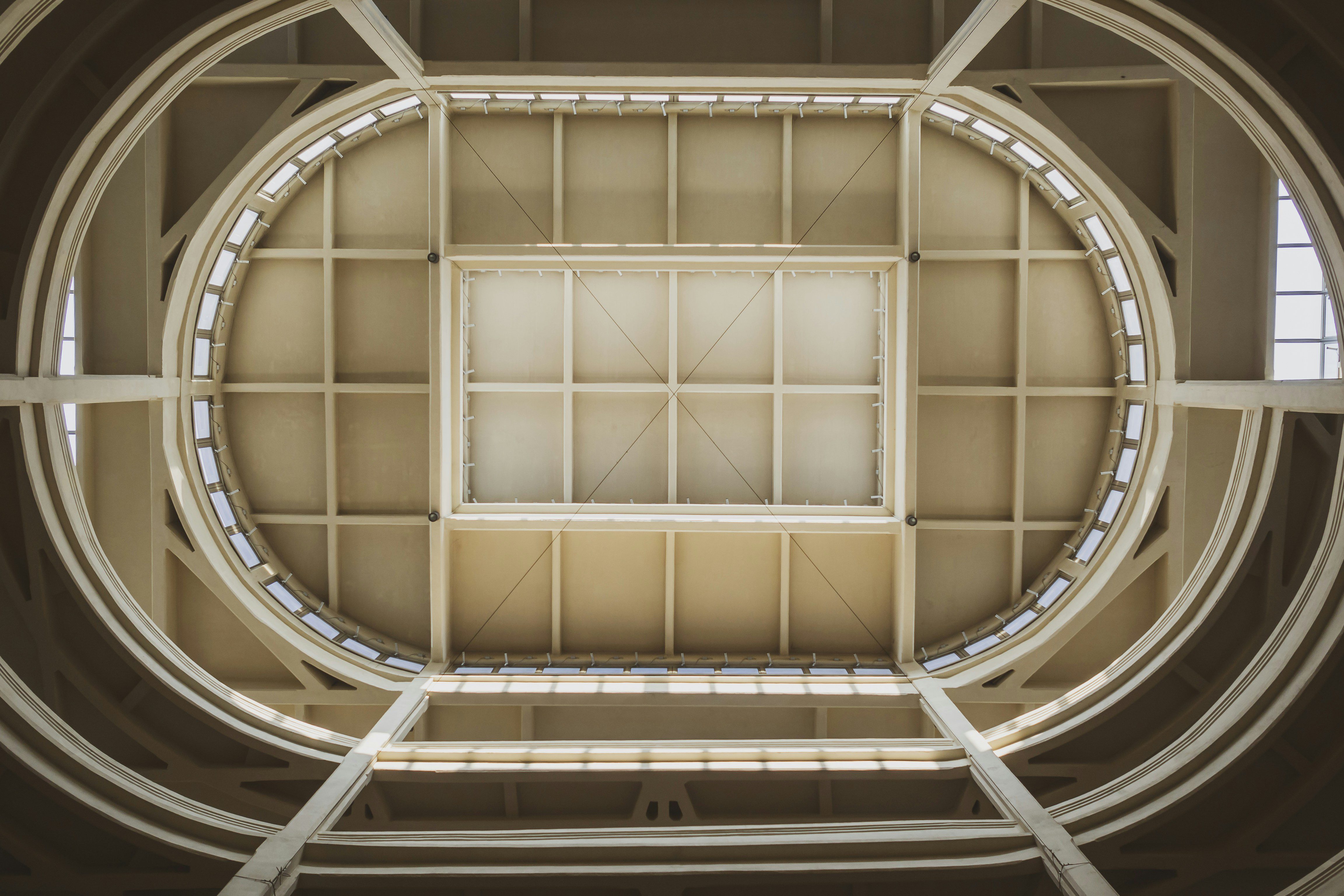 View looking up at a geometric skylight set in a rectangular ceiling, surrounded by oval and rectangular architectural details with natural light streaming in.